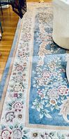 Portion of blue floral oriental rug laid on hardwood floor showing border pattern
