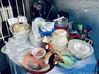 Overview image showing multiple plastic utensils, bowls, decorative trays including horse head and floral design, glass bowls and plastic containers stacked on table