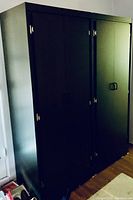 Two black wood wardrobe closets standing side by side with closed doors and metal handles.