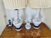 Two white porcelain floral lamps with embossed flower bases and one small floral porcelain vase between them on wooden table