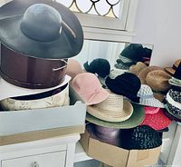 Black wide-brim felt hat on top of a brown hat box, and a collection of assorted hats on a shelf beside a mirror.