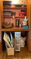 Full view of wooden shelving unit holding various paint bottles, craft tools, and stacked paper supplies