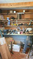 General workshop shelving and workbench cluttered with woodworking items, tools, scrap wood, and containers.