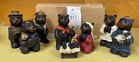Full set of eight black bear nativity figurines including baby in manger, Mary, Joseph, three wise men, and two shepherds with sheep against cardboard background