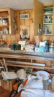Workbench with paint cans, chemical bottles, paper stacks, fan cover and Stihl chainsaw amid cloth bags