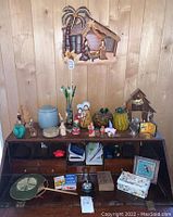 Photo showing wooden cubby shelf against wood panel wall with assorted decorative figurines and nativity items, glass pumpkins, and other small decor.