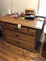 Front view of wood dresser showing top surface and drawer fronts with scratches and contents on top (pins, thread box, scissors).