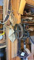Vintage drill press mounted on wooden board with a leather tool belt hanging beside it, showing overall setup and condition.