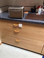 Hamilton Beach stainless steel toaster on kitchen counter with wooden drawers below.