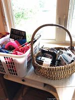 Full view of the lot on a table near a window, includes laundry basket with fabric, woven basket with sewing machine and CDs