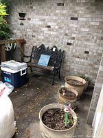 Outdoor bench, Igloo cooler, and garden pots arranged outside against a brick wall