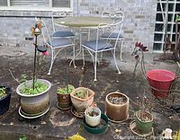 Full view of a round patio table with four matching chairs and multiple garden pots and outdoor decor arranged in front of a brick wall