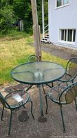 Outdoor round glass top table and four matching mesh metal chairs on concrete patio