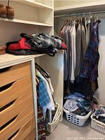 Closet view showing folded clothes on shelves, hanging wool sweater, shirts, flannel and pants, and laundry baskets with more clothing