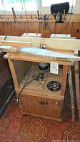 Full view of the portable cable router setup in wooden cabinet with assorted tools visible on wall behind and a mounted circular router bit at center.