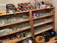 Wooden shelves filled with numerous glass mason jars, glass bottles, vintage cans, and a wooden wine rack on top holding corked bottles.