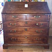 Front view of wooden secretary desk showing two small top drawers and three larger lower drawers with brass handles and keyholes.