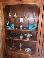 Full view of wood shelf containing turquoise gecko bookends, glass decorative items, silver plate bowl and candle holders.