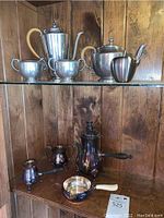 Full display showing an assortment of silver and silverplated coffee and teapots, sugar bowl, creamer, and the sterling silver sauce pan with ivory handle on bottom shelf.