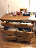 Wooden dresser with sewing notions on top including pin cushions, threads, thimble, heart mirror, and cotton cones. Dresser drawers are open showing additional items but not included.
