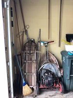 View of two vintage wooden sleds, Toro tiller, broom, and various long-handled garden tools stored together in garage corner.