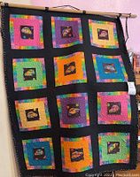 Full view of quilt hanging on wooden rod showing overall pattern of colorful Volkswagen Beetle squares on black background