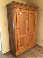 Three-quarter left-front view of the pine armoire showing exterior panels and base.