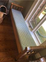 Full side view of antique wooden day bed with blue patterned mattress, showing length and placement next to window.