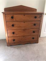 Front view of dresser showing triangular backsplash, four drawers with black round knobs, scalloped base
