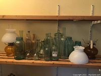 Shelf with assortment of vintage glass bottles and jars, plus two oil lamps with hobnail milk glass shades and amber bases