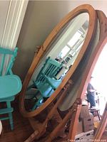 Full view of the pine cheval mirror standing with oval glass and wooden frame on four legs showing its size and shape.