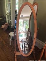 Full view of the pine cheval mirror showing its oval shape, frame, and base on wood flooring.