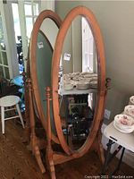Full view of the pine cheval mirror showing the oval mirror and wooden frame with finial capped vertical supports and curved legs on wood floor.