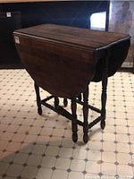 Front angled view of wooden gate leg table folded down, showing drop leaves and turned legs.