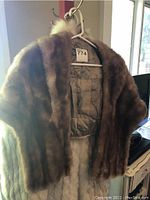 Front view of brown mink stole hanging on hanger, showing fur texture and satin lining inside.