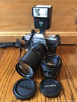 Front view of Minolta SRT-201 camera with 100-200mm zoom lens attached, 50mm lens and lens caps displayed in front, and Sunpak auto 118 flash mounted on camera hot shoe.