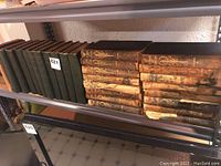 Shelf of vintage books, mostly dark green hardcovers and a stack of worn brown leather-bound volumes.