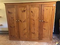 Front view of four-door pine armoire showing doors closed, knob hardware and natural finish.