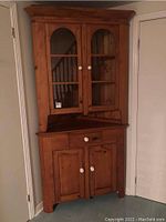Front view of two-piece pine corner cabinet showing upper glass doors, lower drawer and doors