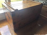 Angled side view of antique pine trunk showing side rope handle and wood joinery with marks and scratches.