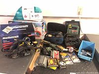 Wide view of entire lot showing tools and accessories on tabletop including sander, planer in box, Bissell Spot Lifter, stapler, saw, and miscellaneous supplies.
