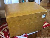 Front and side view of the closed vinyl record storage trunk with a faux leather tan finish and embossed detailing on top.