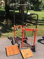 Two orange steel dollies with wooden platforms outdoors, showing full height and structure.