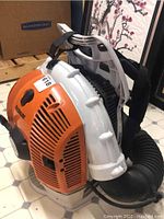 Front-quarter view of backpack housing and attached blow tube, showing overall unit shape and strap layout