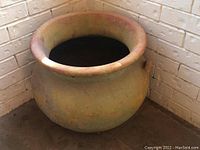 Front view of the terra cotta planter urn placed in a corner showing the rounded body and wide rim.
