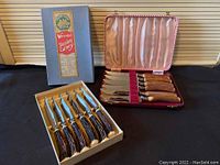 Two sets of steak knives, one boxed set with faux stag handles, one in silk-lined case with brown handles