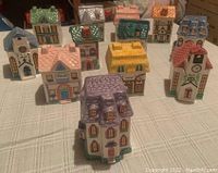 Front group view of 12 colorful Avon glass spice containers shaped as houses on tablecloth
