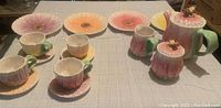 Full set displayed on table showing dessert plates, cups with saucers, teapot, creamer, and sugar container with floral and bee design.