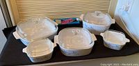Full set of Corning Ware Iris pattern casseroles with lids and handle displayed on black cloth.