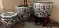 Three ceramic urns grouped together showing decorative patterns and wood stand